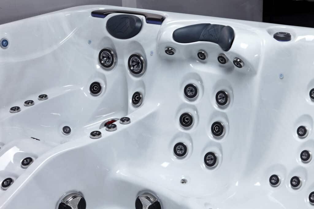 Vue rapprochée d'un jacuzzi blanc avec de multiples buses de massage chromées, appuie-têtes noirs et commandes de contrôle intégrées dans la coque.