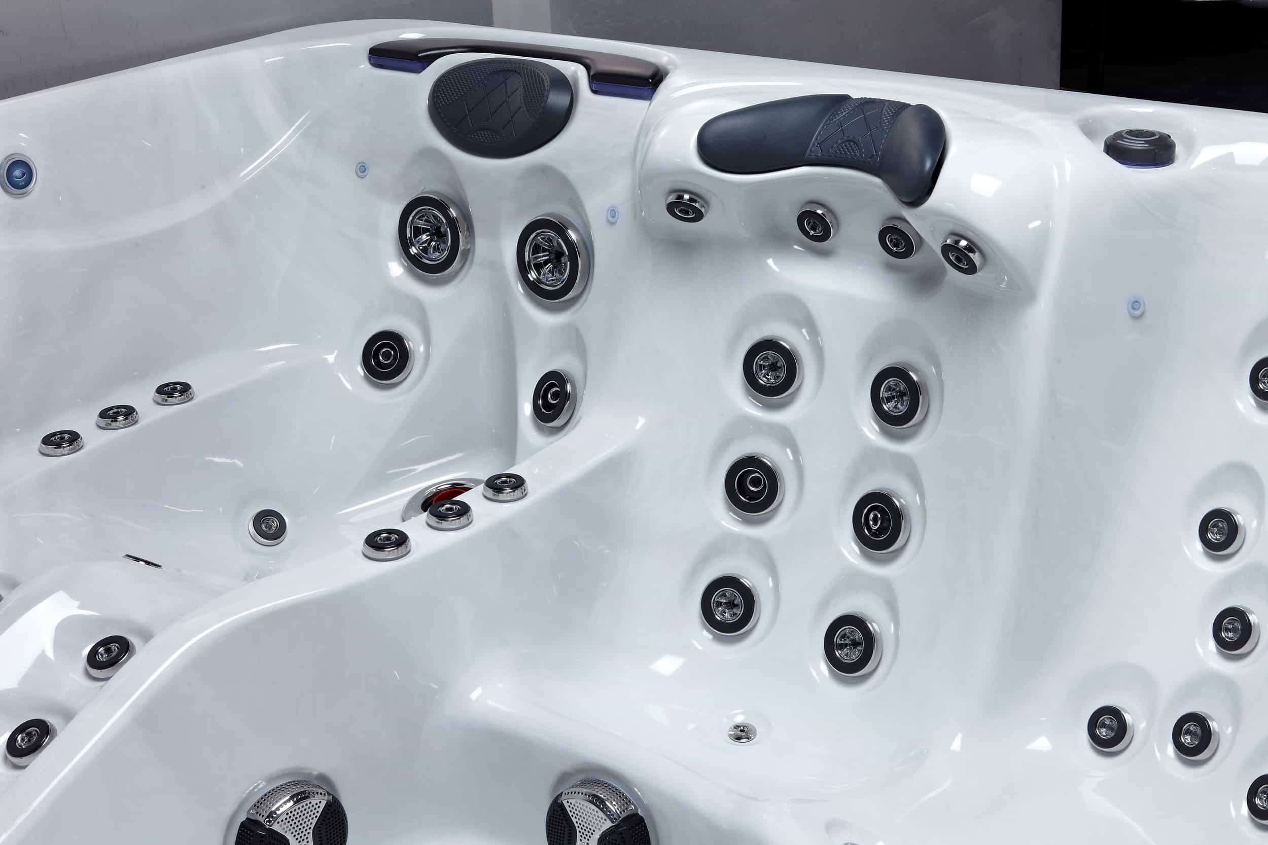 Vue rapprochée d'un jacuzzi blanc avec de multiples buses de massage chromées, appuie-têtes noirs et commandes de contrôle intégrées dans la coque.