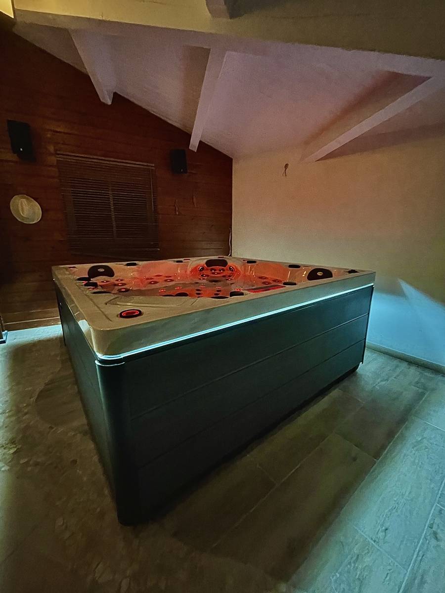 Grand spa intérieur moderne avec jacuzzi lumineux à jets orange dans une pièce aux murs boisés et carrelage clair, offrant détente et luxe.