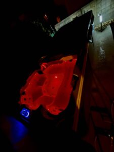 Jacuzzi extérieur éclairé en rouge vif la nuit, créant une ambiance relaxante. Panneau de contrôle bleu lumineux visible.