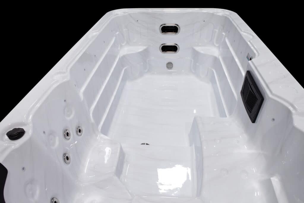 Intérieur d'un spa ou d'une piscine de nage blanche marbrée, montrant des jets chromés, une grille de filtration noire et des marches intégrées.