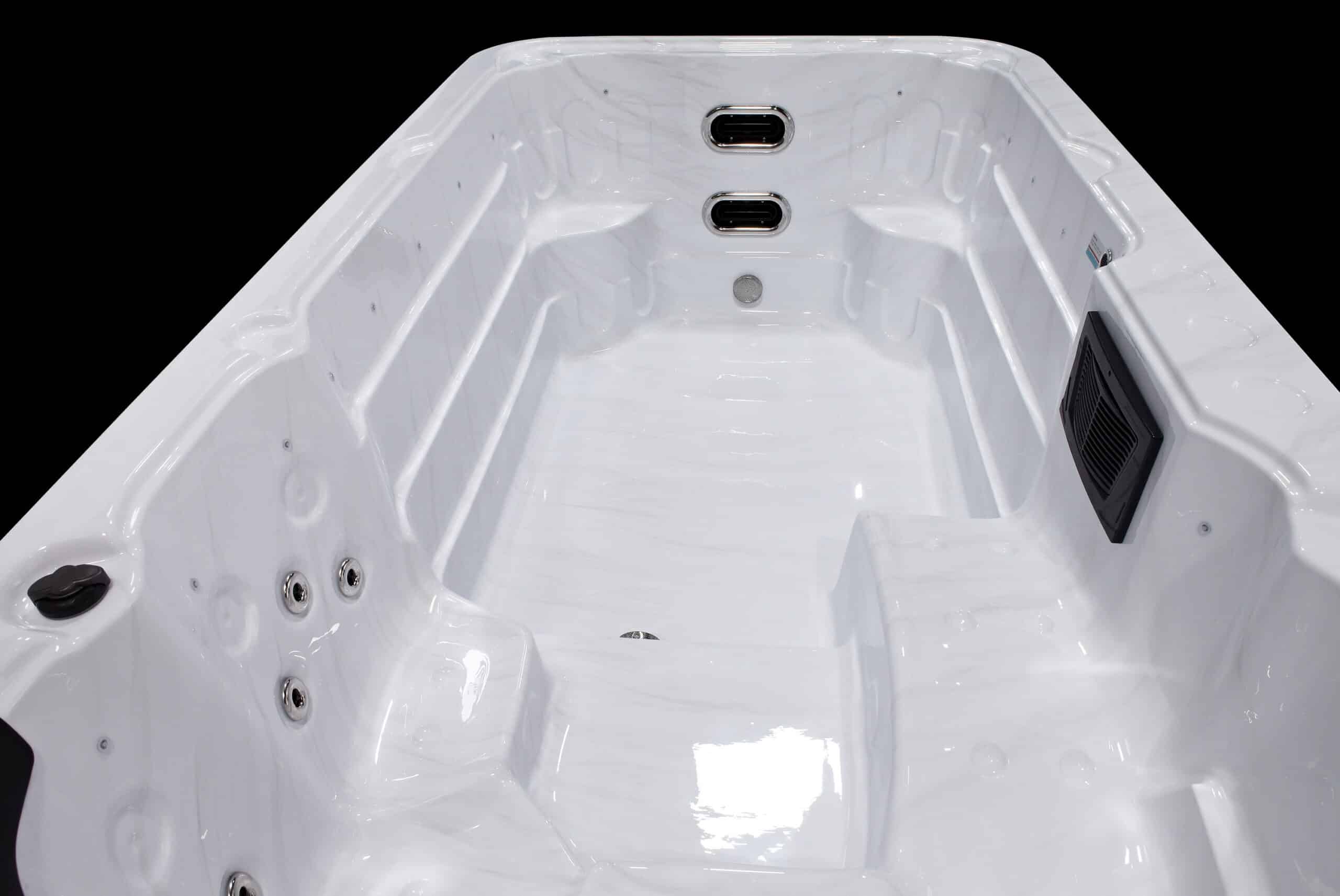 Intérieur d'un spa ou d'une piscine de nage blanche marbrée, montrant des jets chromés, une grille de filtration noire et des marches intégrées.