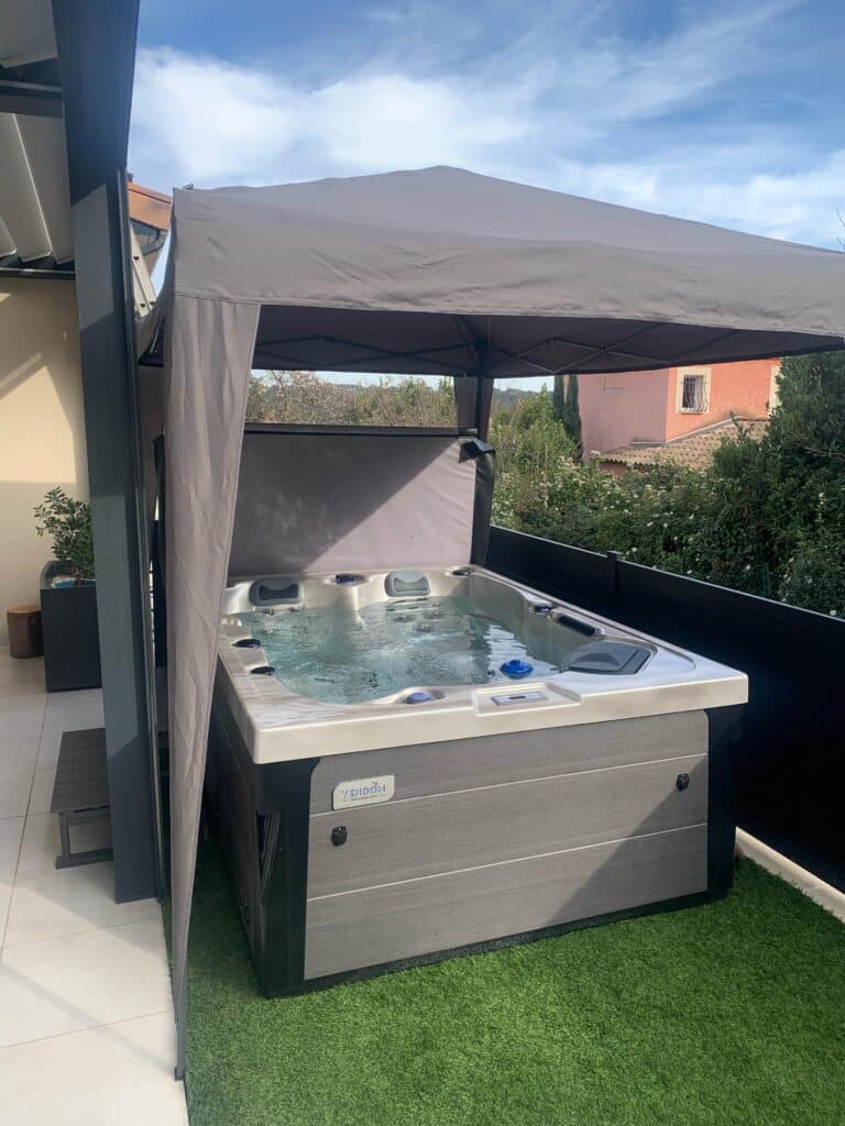 Spa Jacuzzi VENDOM : installation sur terrasse et détente. Spa Jacuzzi VENDOM prêt à l'emploi sur terrasse carrelée et gazon artificiel, abrité par une tonnelle. Pour un moment de bien-être.