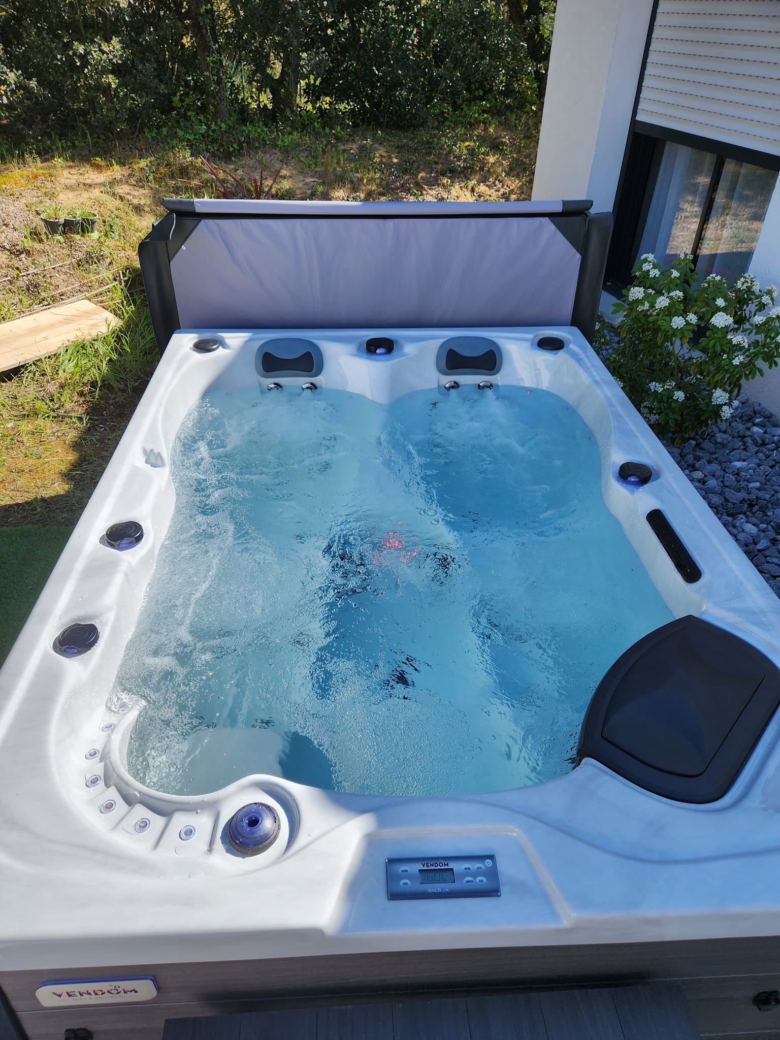 Spa Vendom extérieur en fonctionnement avec de l'eau bleue moussante. Le panneau de contrôle Balboa affiche la température.