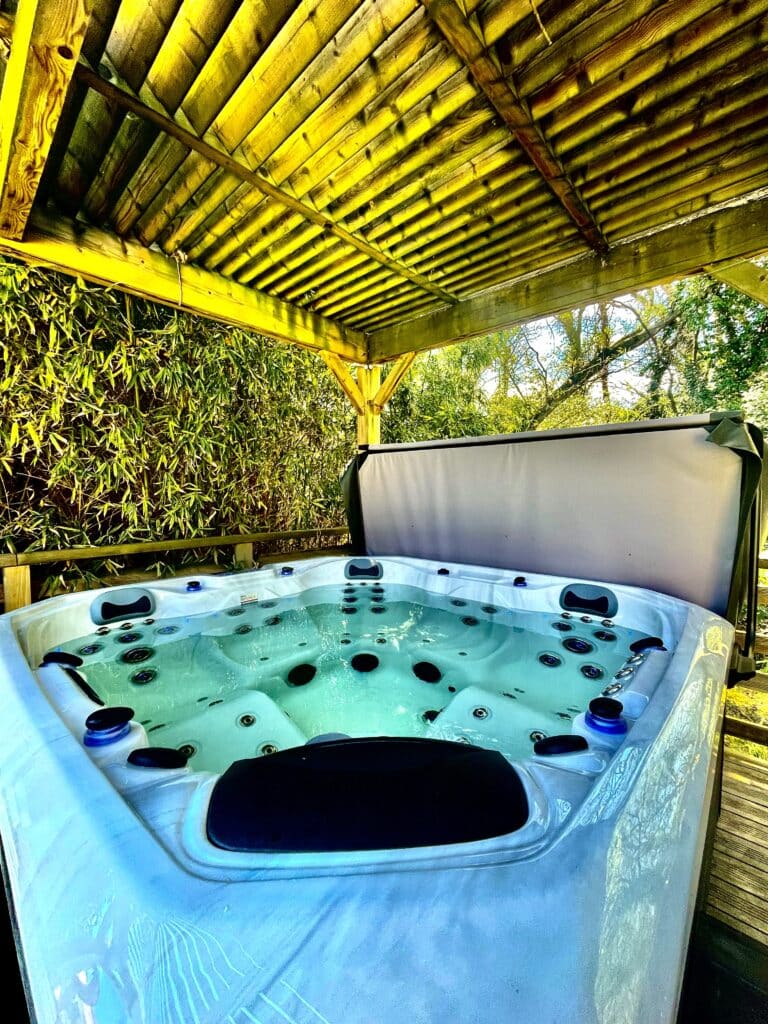 Spa bouillonnant extérieur sous une pergola en bois jaune vif. L'eau turquoise reflète les lumières, entouré de bambous.