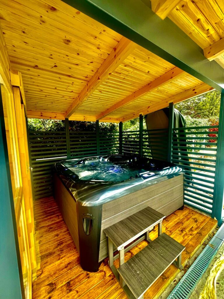 Jacuzzi extérieur privé : abri bois design, vert forêt Jacuzzi d'extérieur moderne sous un abri en bois avec plafond lambrissé doré. Murs à lattes vert foncé pour plus d'intimité.