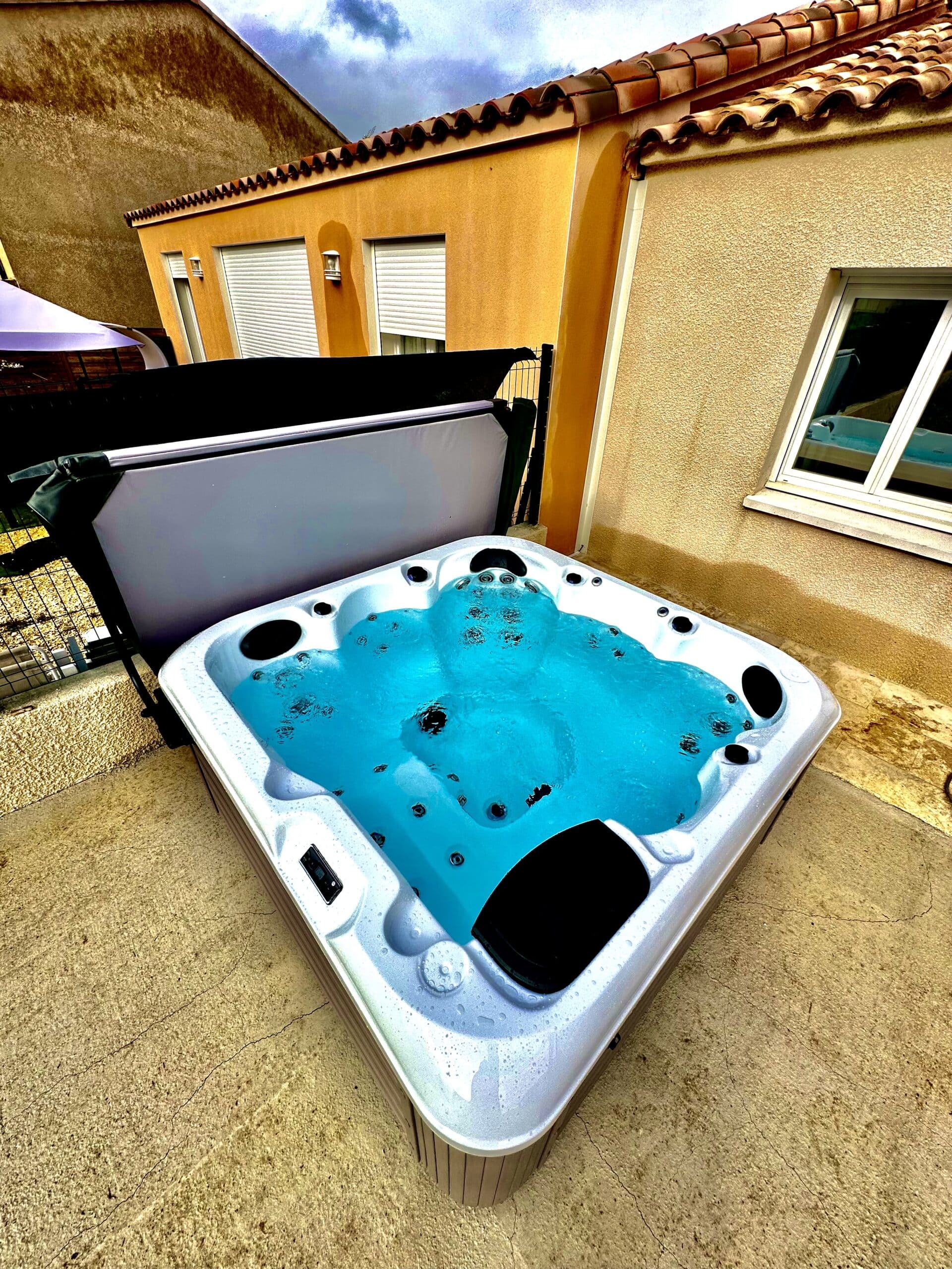 Hot tub moderne extérieur avec eau turquoise bouillonnante sur terrasse en béton. Arrière-plan de bâtiments ocre et toit tuiles.