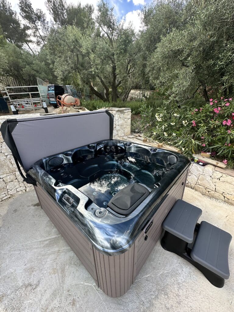 Spa de luxe moderne extérieur Vendom, coque marbrée foncée. Le couvercle gris est levé, révélant l'eau pétillante sous un ciel bleu.