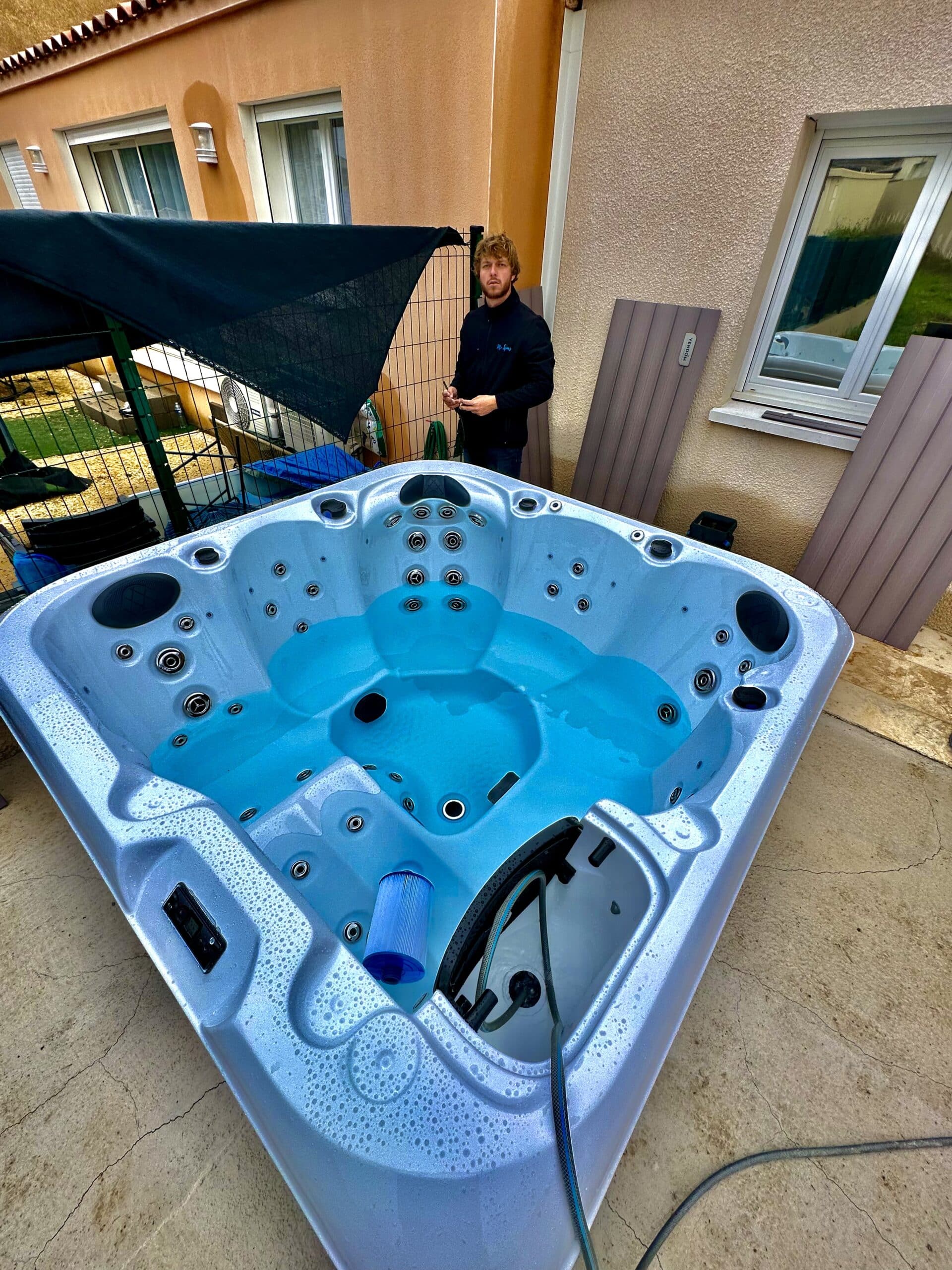 Technicien Mr. Spa nettoyant un grand jacuzzi extérieur Vendom bleu. Le filtre et les panneaux latéraux sont retirés sur le patio.