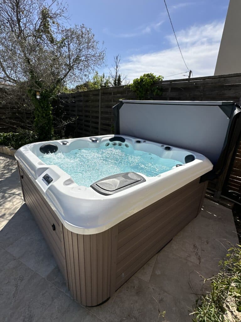 Jacuzzi extérieur en plein soleil : détente et bulles Jacuzzi spa moderne d'extérieur, coque blanche et habillage bois, dont l'eau bleue bouillonne sur une terrasse ensoleillée.
