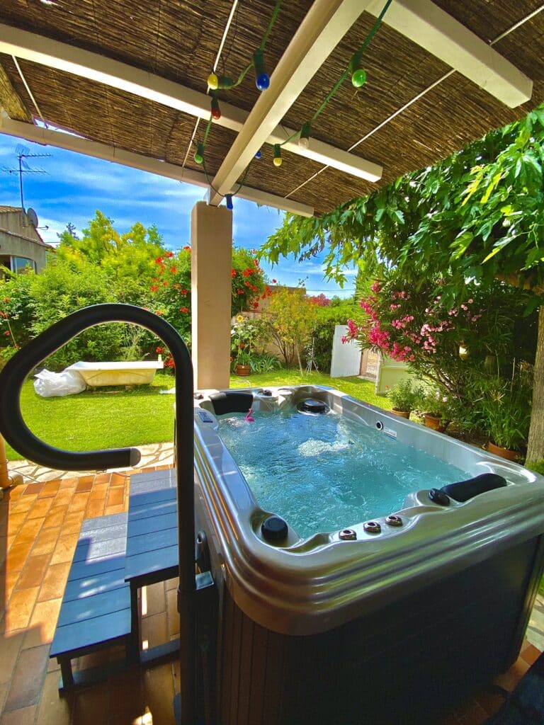 Détendez-vous ! Jacuzzi extérieur dans jardin tropical Spa extérieur bouillonnant sous une pergola. Végétation luxuriante, fleurs rouges et roses, carrelage en terre cuite.
