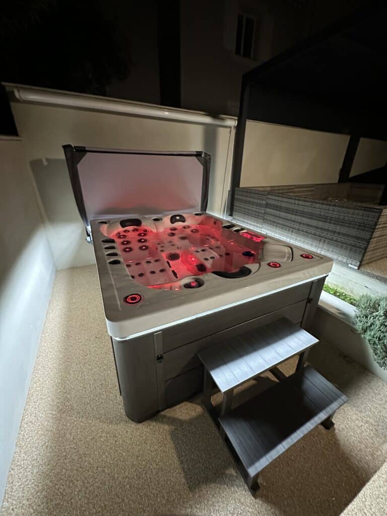 Jacuzzi extérieur moderne la nuit sur terrasse claire, doté d'un éclairage subaquatique LED rouge vif. Des marches grises y mènent.