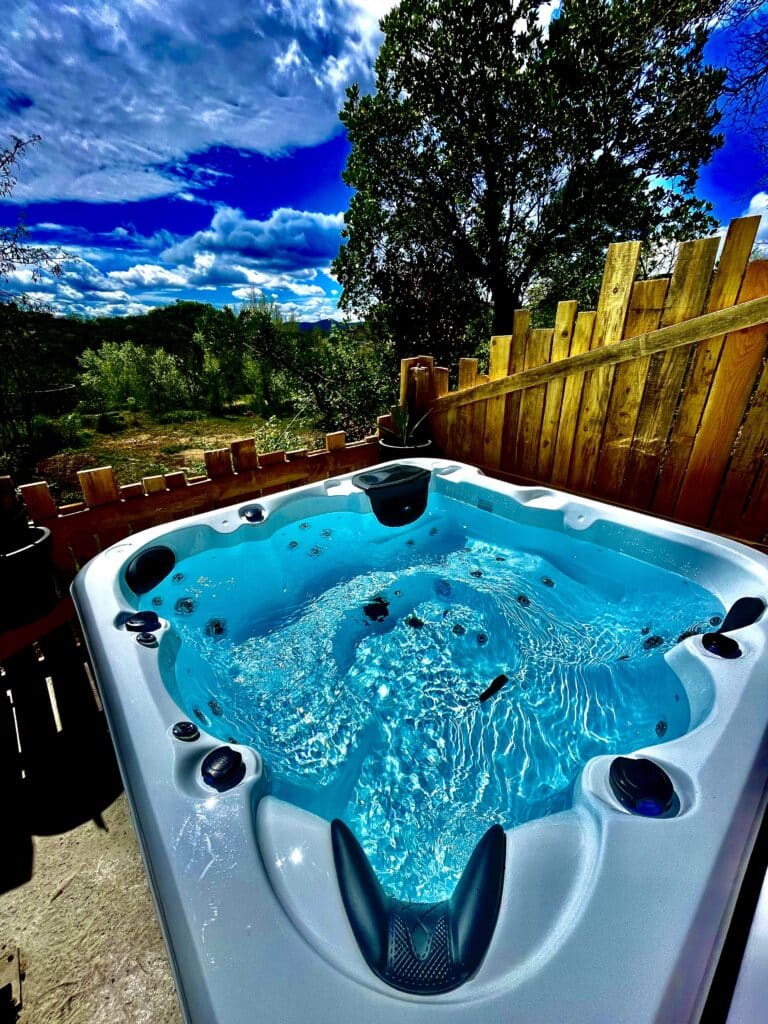 Grand jacuzzi extérieur moderne rempli d'eau turquoise bouillonnante. Vue sur la forêt et les collines sous un ciel bleu dramatique.