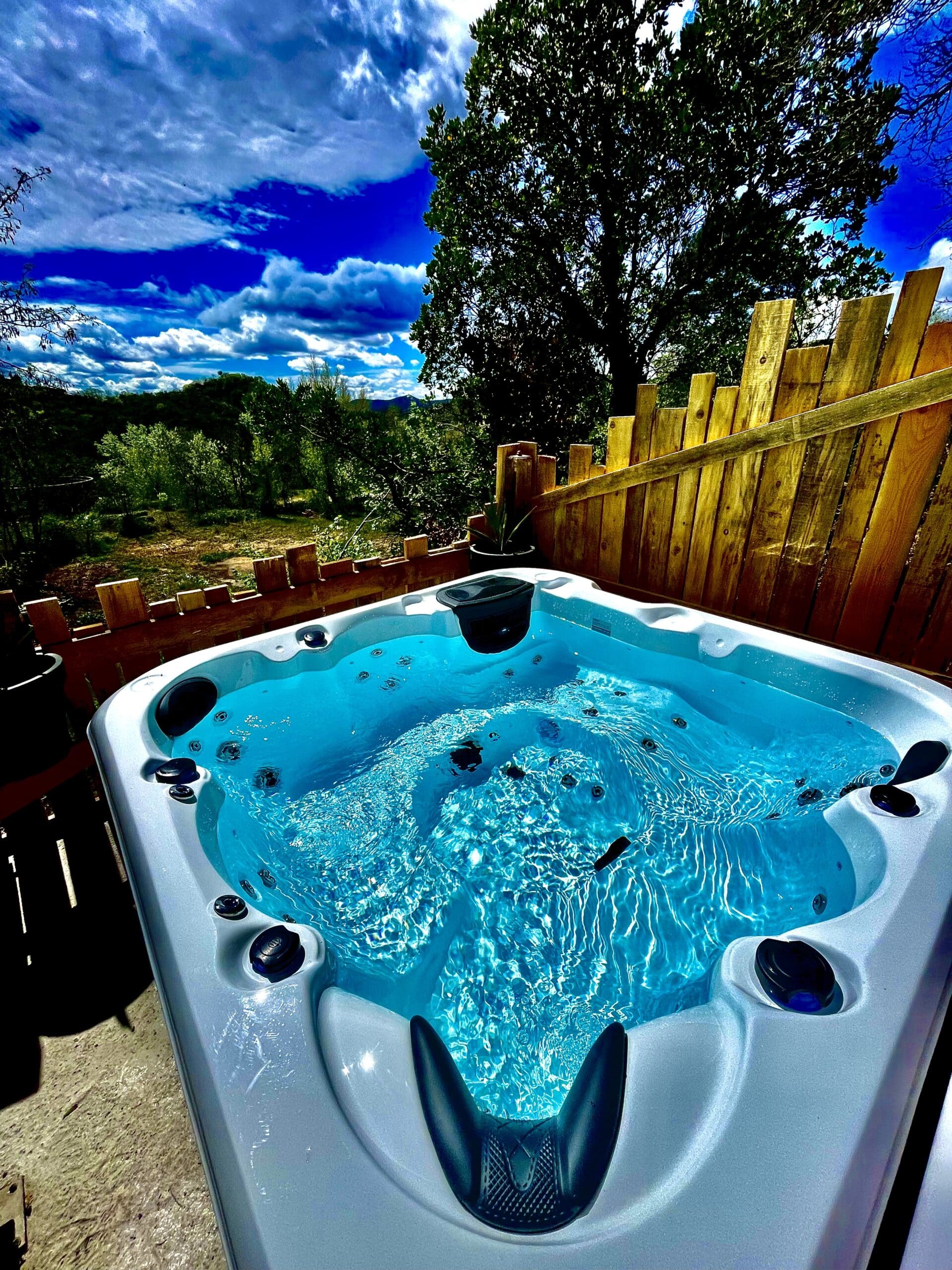Grand jacuzzi extérieur moderne rempli d'eau turquoise bouillonnante. Vue sur la forêt et les collines sous un ciel bleu dramatique.