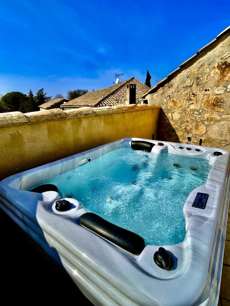 Jacuzzi extérieur : Détente et luxe sous un ciel bleu éclatant. Jacuzzi moderne à la coque marbrée sur une terrasse ensoleillée. L'eau turquoise bouillonne face à un mur de pierre et un ciel bleu éclatant.