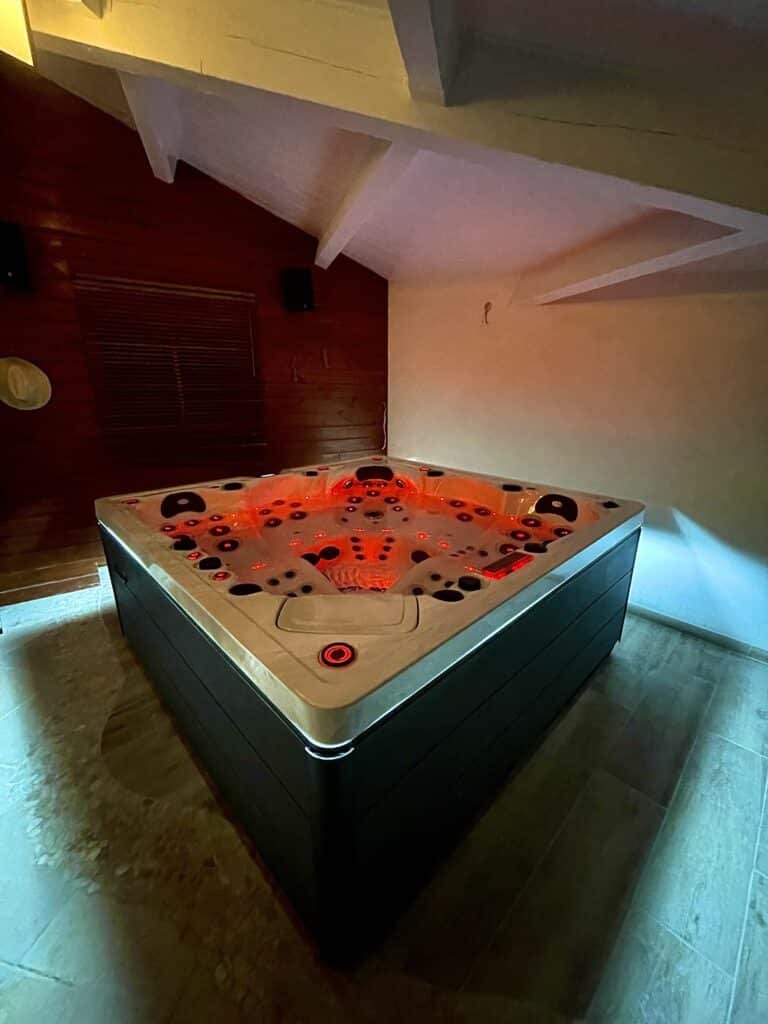 Spa intérieur de luxe : ambiance romantique LED rouge Spa de luxe carré avec éclairage chromothérapie rouge vif dans une pièce avec murs en bois et poutres apparentes.