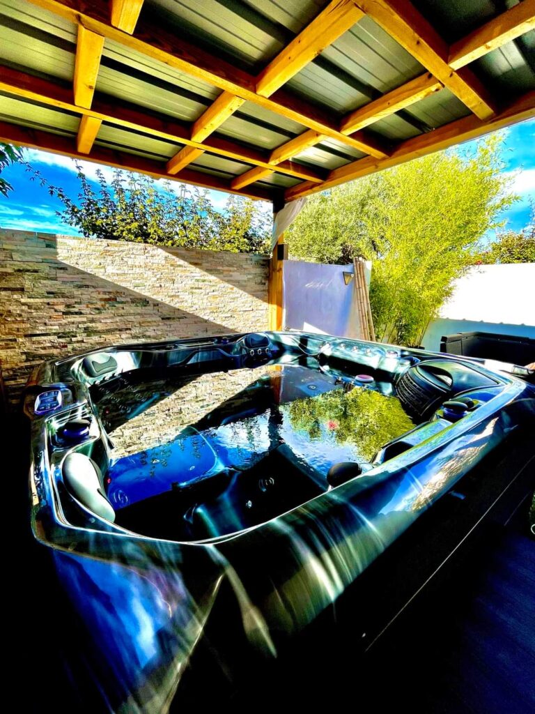 Jacuzzi extérieur moderne : détente sous la pergola bois. Magnifique jacuzzi extérieur sous une pergola en bois. Les reflets de l'eau révèlent un mur de pierre et un feuillage luxuriant, invitant à la détente.
