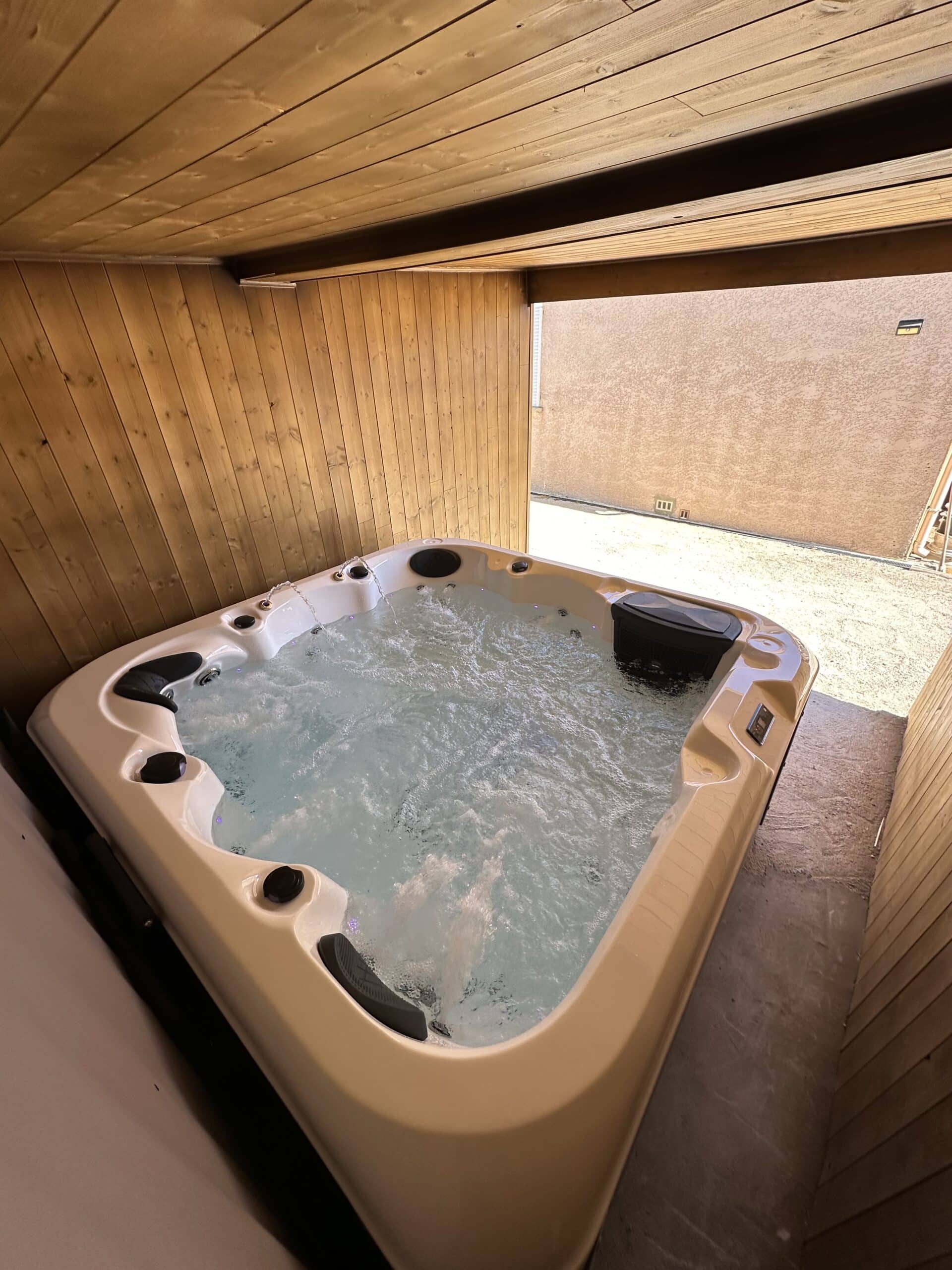 Spa jacuzzi extérieur moderne et bouillonnant, installé dans un coin privé avec murs et plafond recouverts de lambris en bois clair.