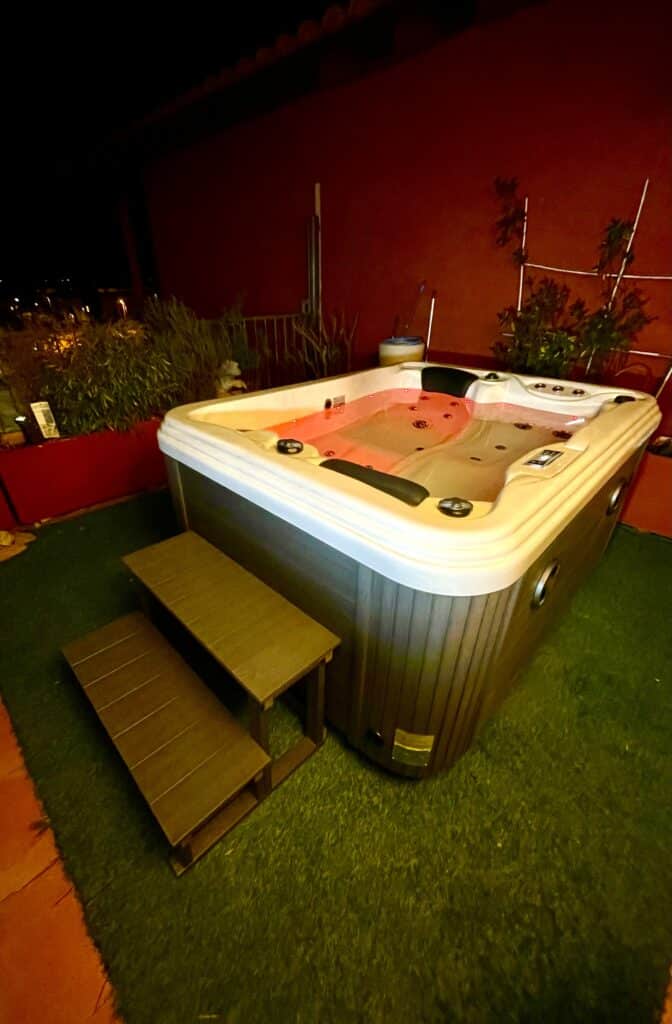 Jacuzzi et spa extérieur: luxe et détente la nuit. Grand jacuzzi spa extérieur illuminé en rouge la nuit, posé sur gazon synthétique avec marches d'accès, ambiance cosy et détente.