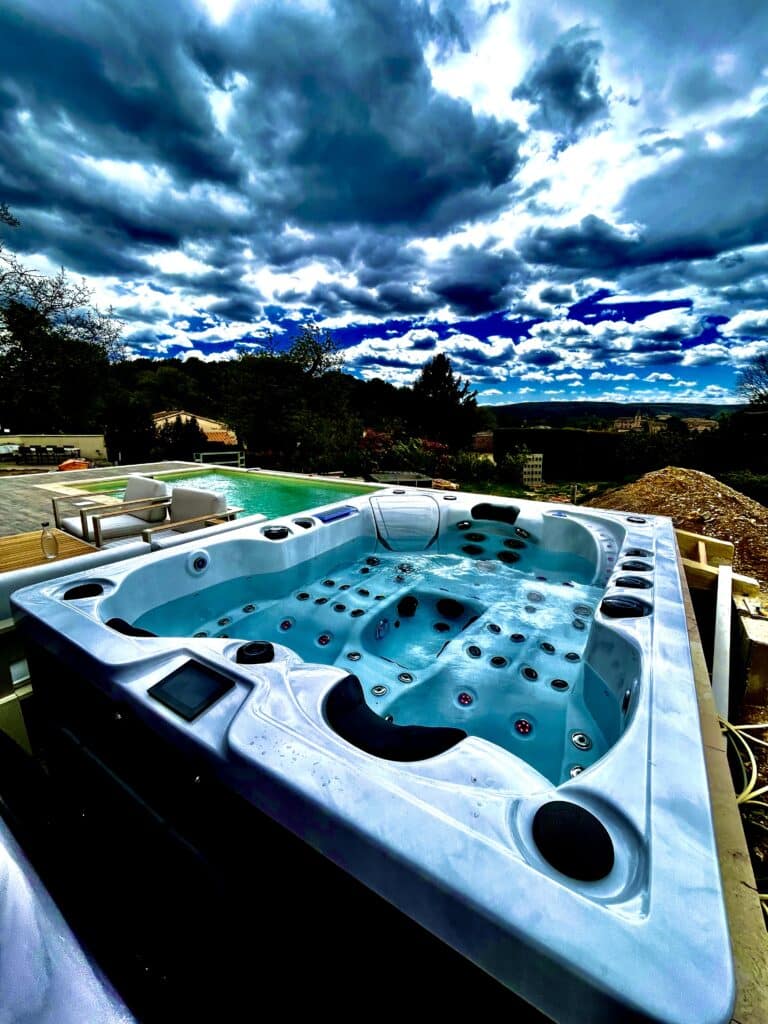 Jacuzzi de luxe extérieur sous un ciel bleu orageux. Jacuzzi bouillonnant blanc, installé près d'une piscine extérieure de luxe. Ciel orageux bleu foncé spectaculaire au-dessus des collines.