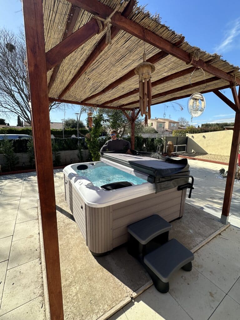 Jacuzzi extérieur et spa sous pergola en bois. Jacuzzi extérieur sous pergola en bois sur une terrasse ensoleillée. Un homme souriant prépare le spa pour la détente.