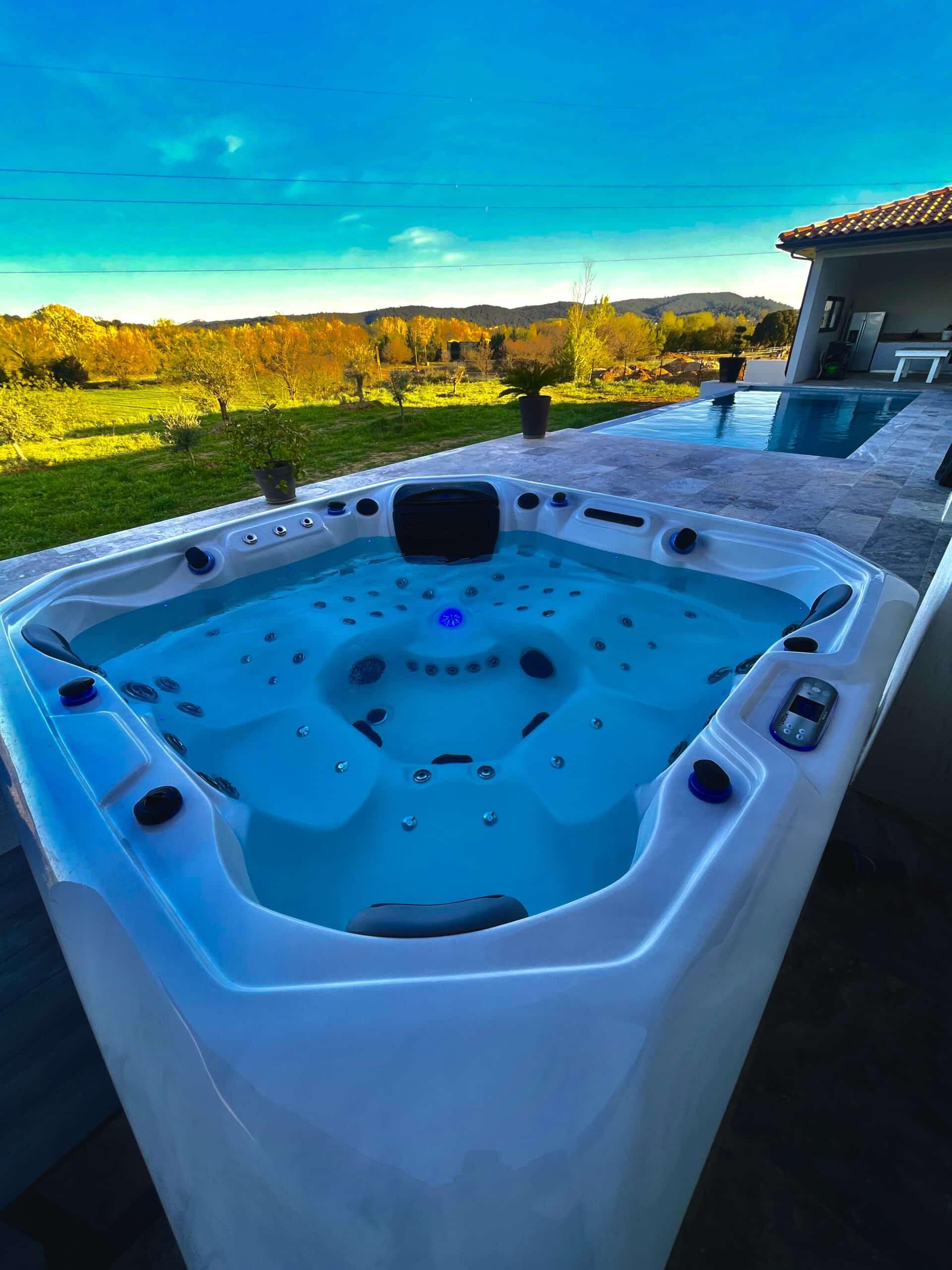 Jacuzzi extérieur moderne et lumineux (lumière bleue) sur une terrasse en pierre. Vue imprenable sur la campagne et les collines.