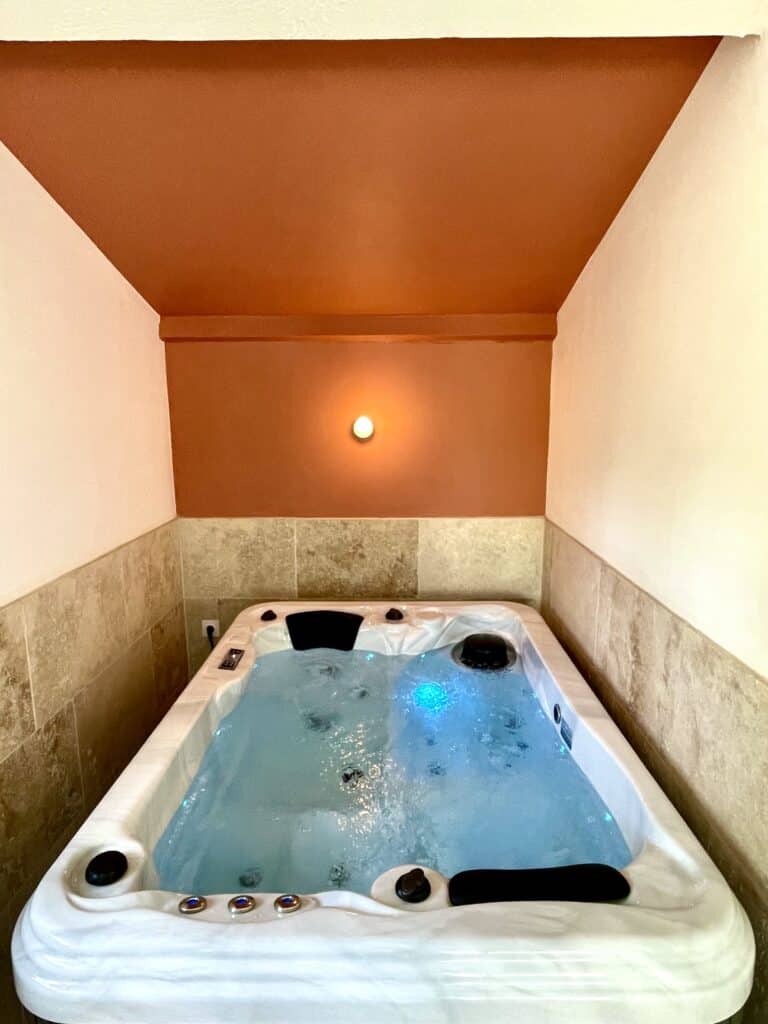 Jacuzzi spa intérieur aux jets actifs, encastré dans une alcôve aux murs terracotta et crème. Ambiance chaleureuse avec éclairage tamisé.