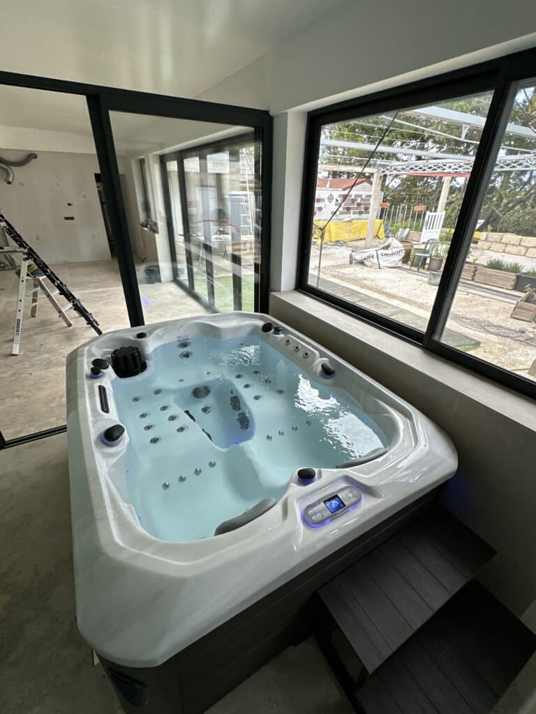 Jacuzzi Vendom en eau, installé dans une pièce en rénovation avec grandes baies vitrées donnant sur l'extérieur.