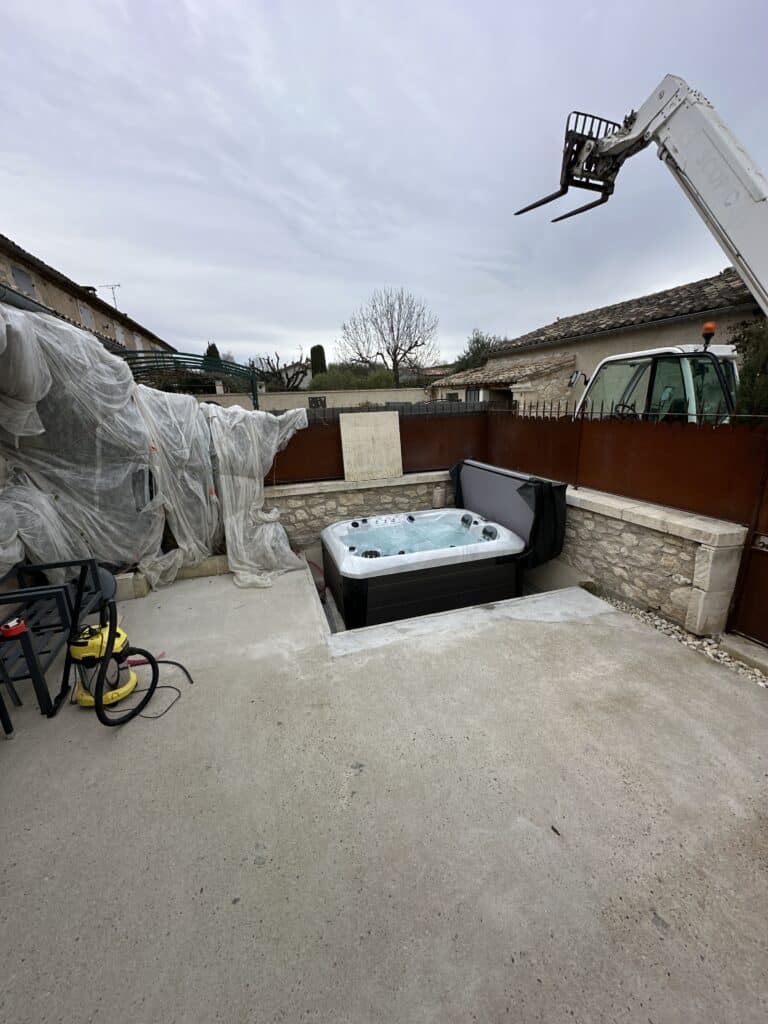 Installation Spa Jacuzzi encastré : projet de terrasse. Installation d'un spa encastré dans une terrasse en béton, entouré de murs en pierre et d'un chantier actif avec un élévateur télescopique (SCOPIC).