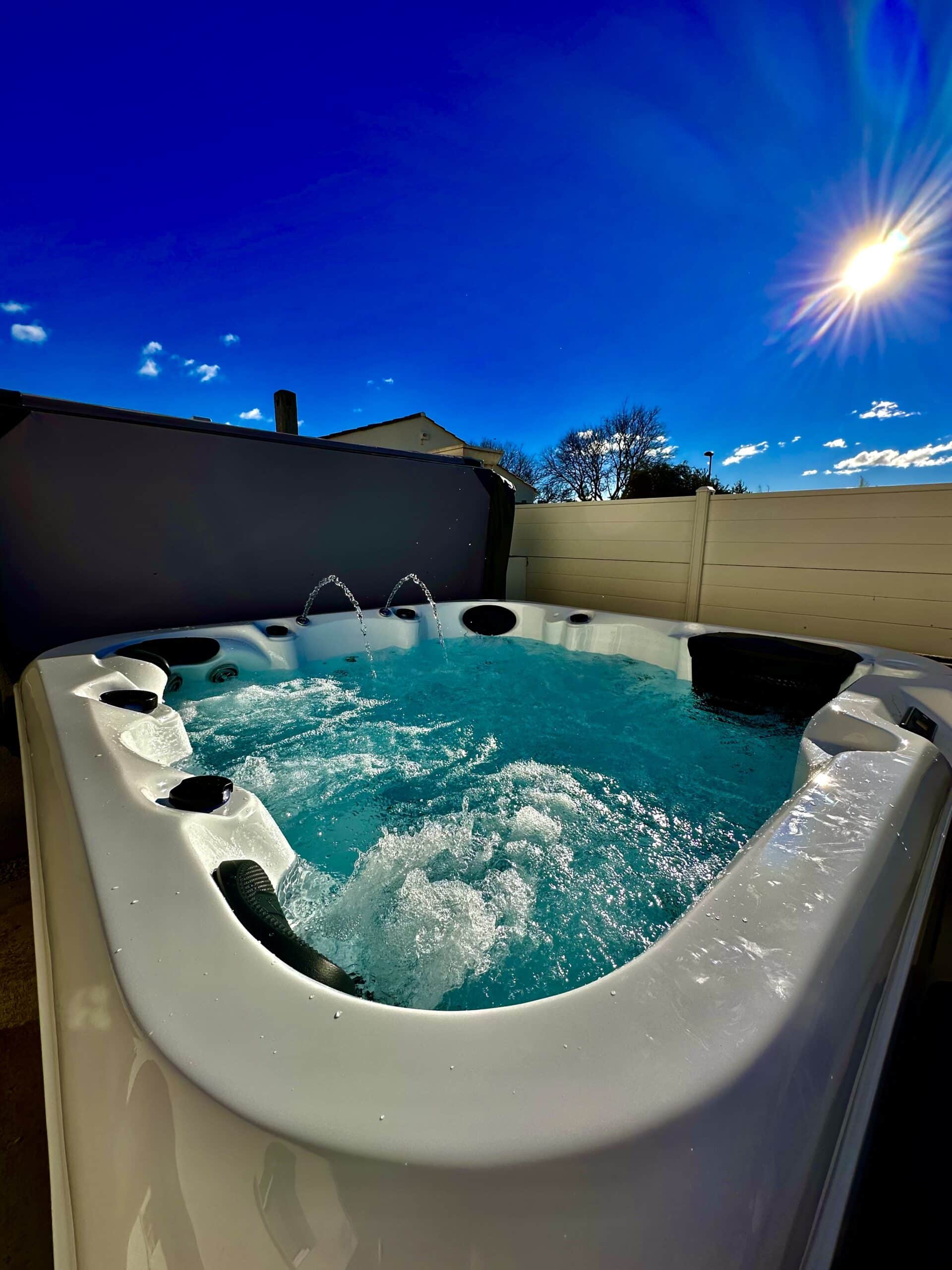 Jacuzzi extérieur blanc bouillonnant, eau turquoise vive et fontaines. Soleil éclatant et ciel bleu cobalt pour une session détente.