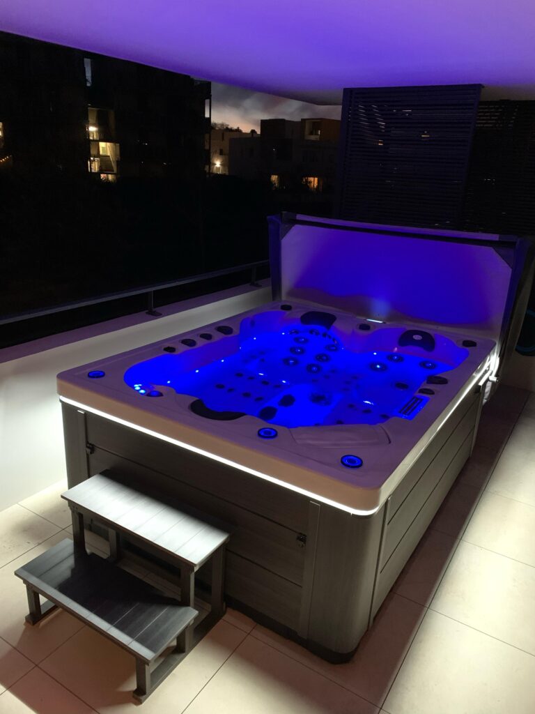 Spa extérieur de luxe : éclairage LED bleu sur balcon Luxueux spa extérieur sur un balcon la nuit, brillant d'un éclairage LED bleu vif et blanc. Étapes d'accès modernes.