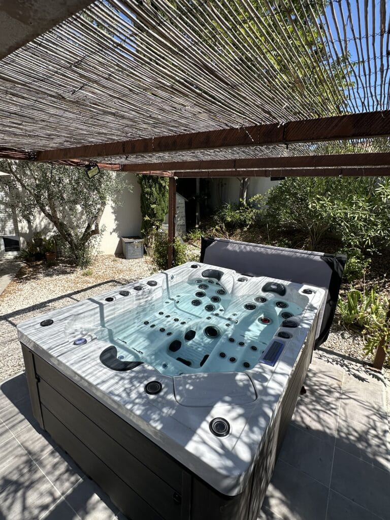 Détente assurée dans ce grand spa extérieur sous une pergola en bambou. Jets visibles, lumière du soleil filtrée.