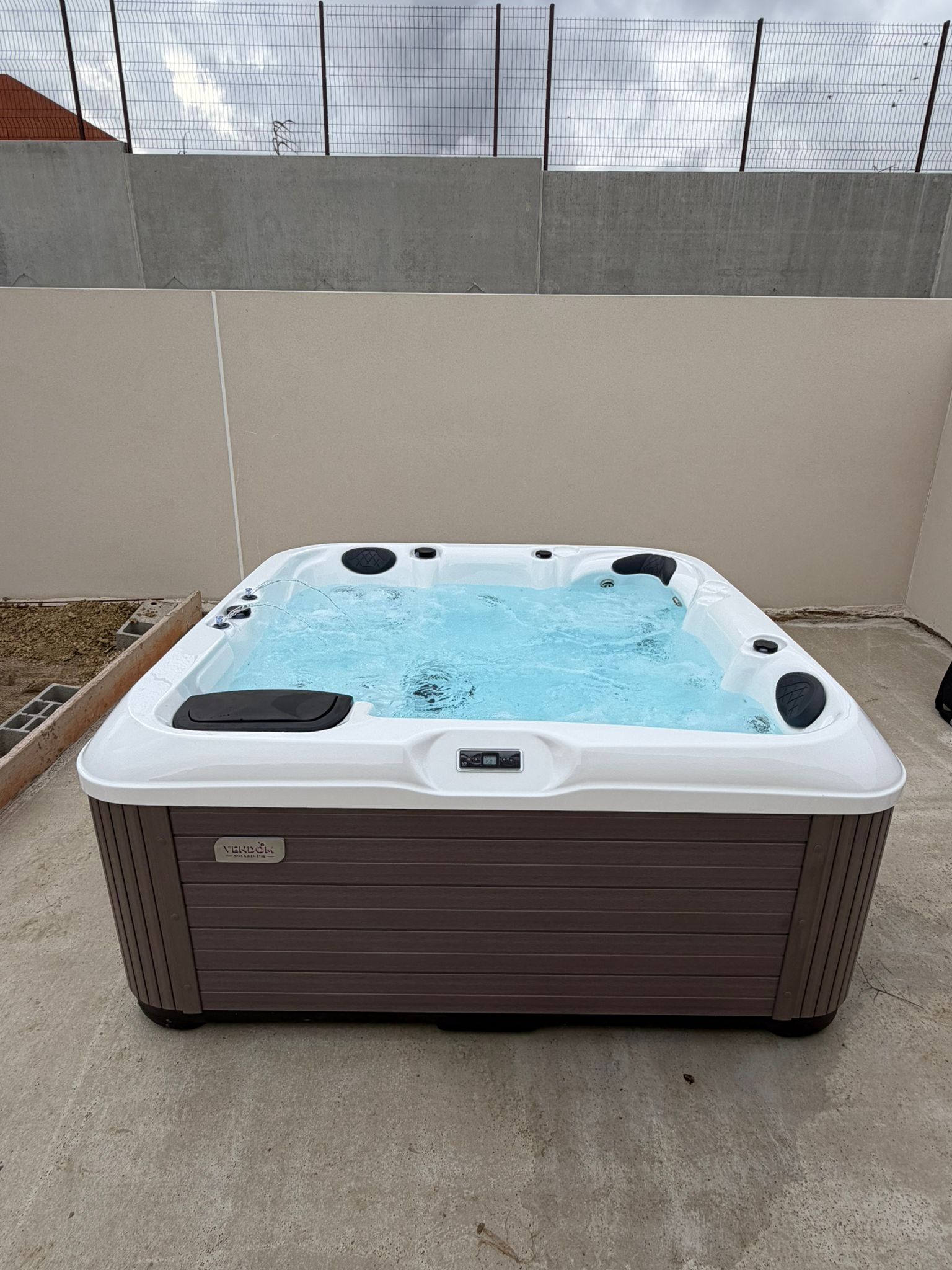 Spa extérieur Verdolm (SPAS & BIEN-ÊTRE) blanc et marron, avec jets actifs, installé sur un patio privé en béton entouré de hauts murs.