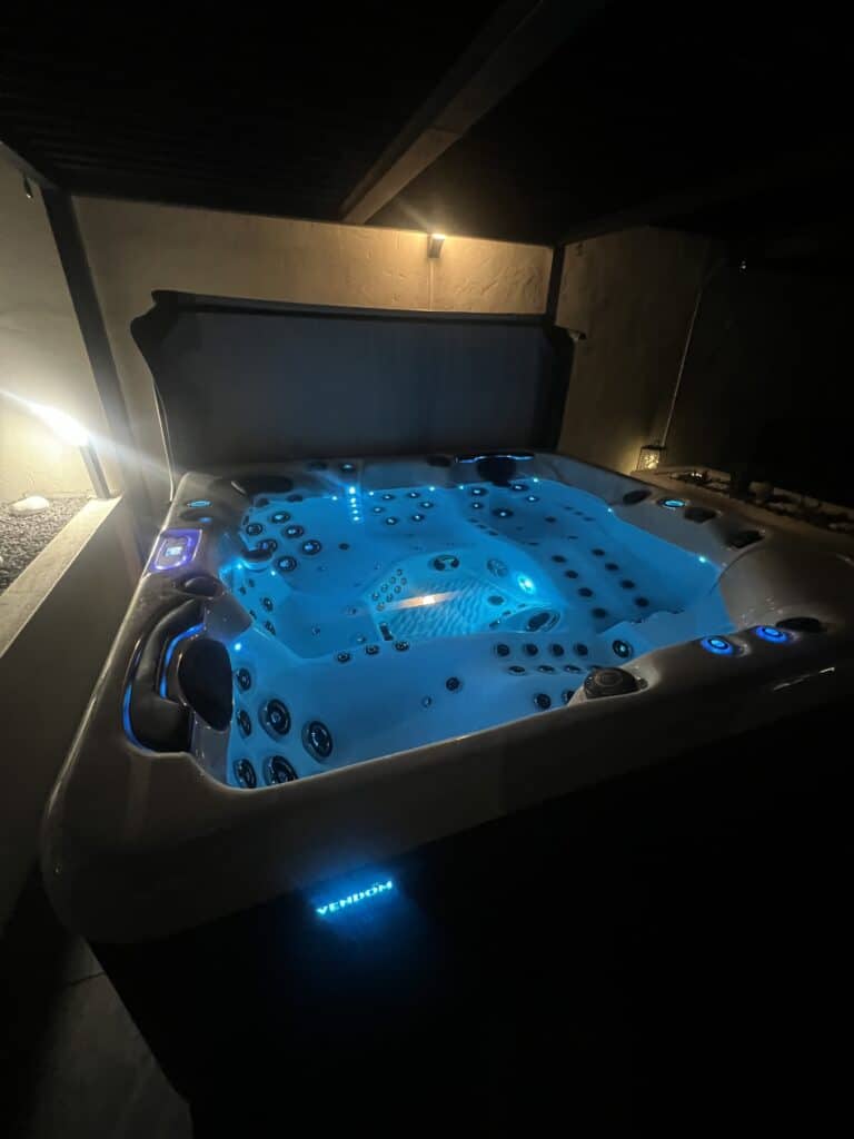 Spa Vendom extérieur de luxe, éclairé en bleu vif par des lumières LED, prêt pour une soirée détente. Texte visible: VENDOM.