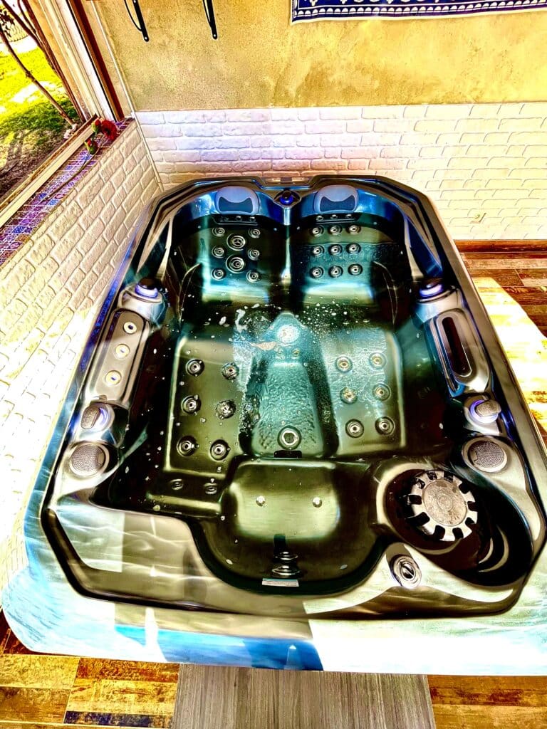 Bain à remous moderne noir avec jets actifs et éclairage LED bleu. Installé contre un mur jaune texturé et une brique blanche.