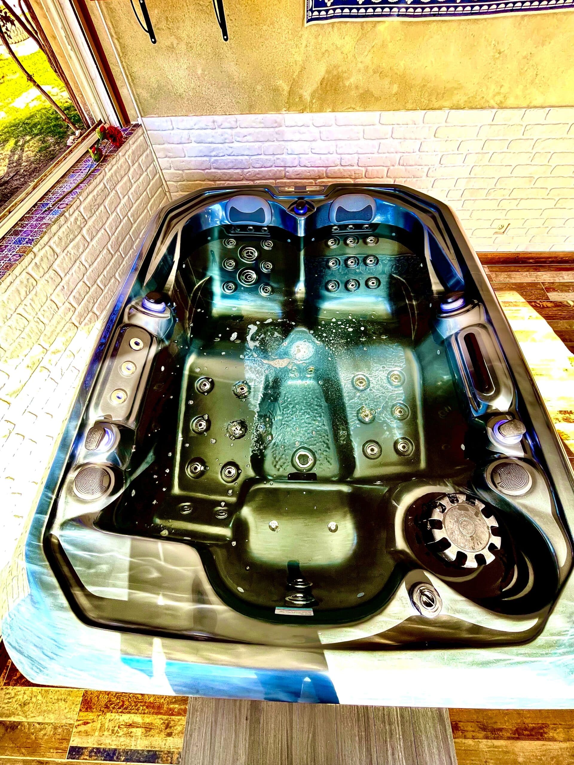 Bain à remous moderne noir avec jets actifs et éclairage LED bleu. Installé contre un mur jaune texturé et une brique blanche.