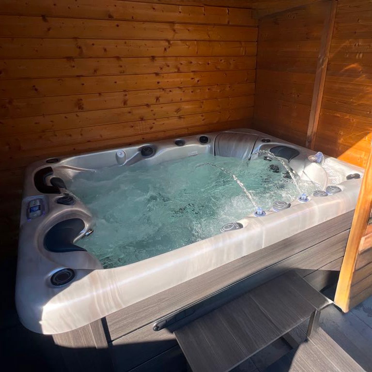 Luxueux spa bouillonnant dans une cabane en bois chaleureuse. Les trois fontaines d'eau et l'éclairage mettent en valeur l'ambiance détente.