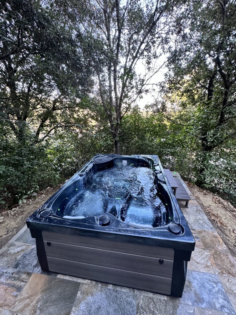 Spa extérieur moderne en forêt | Détente ultime Spa extérieur moderne en fonction, dans un cadre forestier isolé. L'eau bouillonnante est éclairée sur une terrasse en dalles d'ardoise.