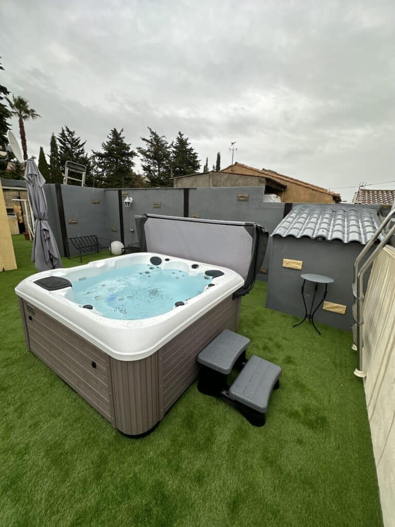 Jacuzzi extérieur moderne sur gazon synthétique Jacuzzi spa extérieur marron ouvert avec marches grises sur gazon artificiel. Ambiance intime sous un ciel couvert.
