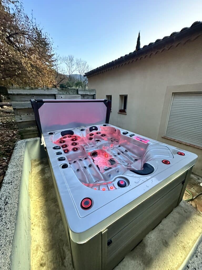 Bain à remous extérieur éclairé en rouge, installé sur une terrasse. Le spa moderne, semi-enterré, offre un moment de détente.