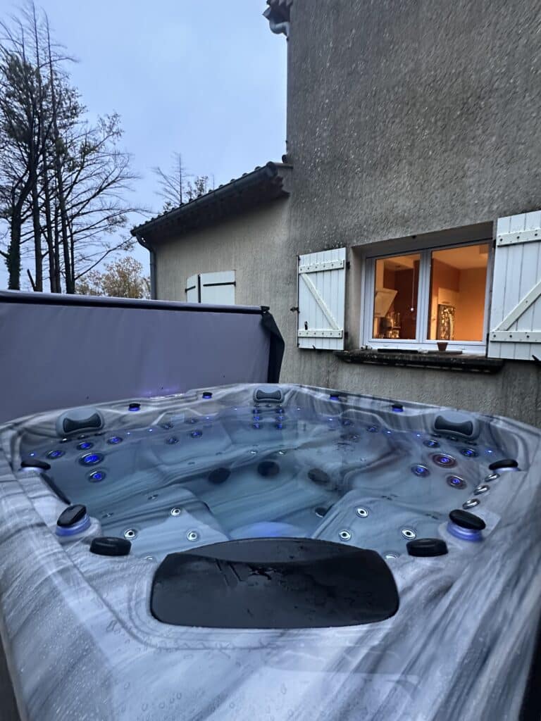 Spa extérieur : L'expérience Jacuzzi de luxe au crépuscule. Luxueux spa d'extérieur au crépuscule. L'eau bleue éclairée contraste avec le mur de stuc et la cuisine intérieure chaleureuse.