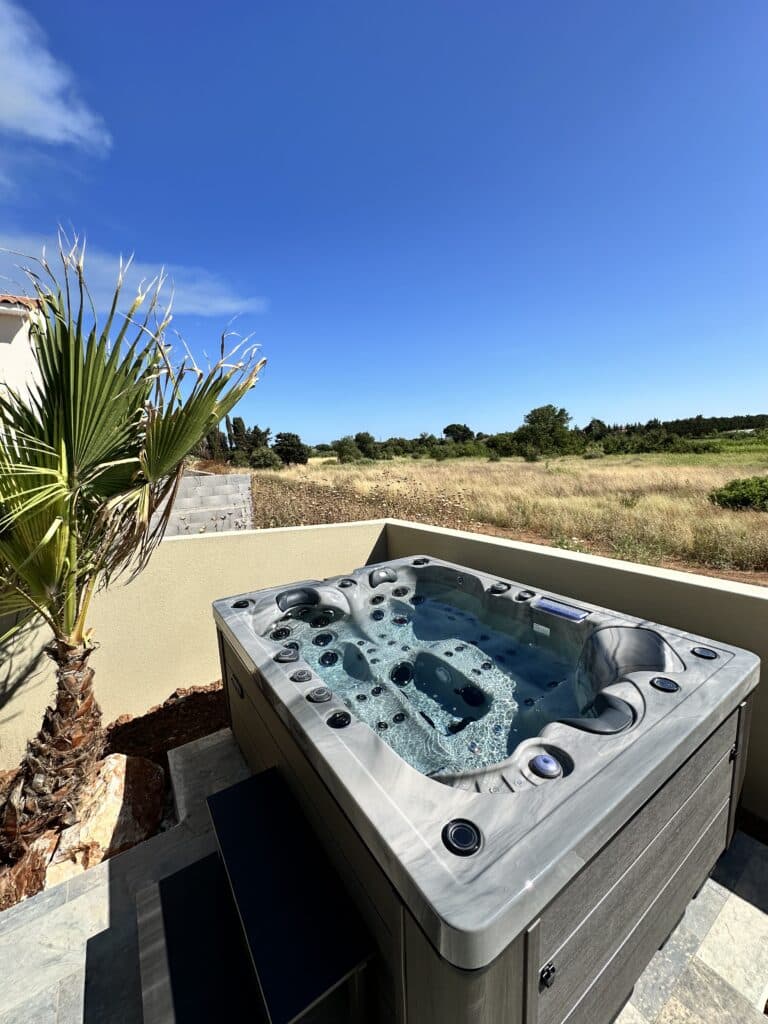 Jacuzzi extérieur moderne sous le soleil et ciel bleu Spa jacuzzi extérieur moderne sur terrasse, à côté d'un palmier. Vue sur un champ sec et un ciel bleu éclatant.