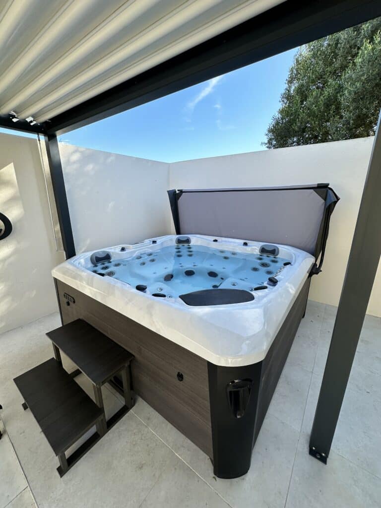 Jacuzzi Spa extérieur moderne pour détente sous pergola. Jacuzzi moderne et spacieux sous pergola. Coque blanche, habillage bois foncé, marches. Espace extérieur privé.