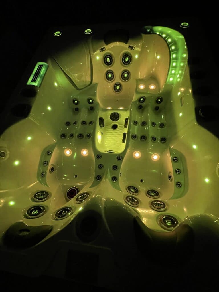 Jacuzzi haut de gamme éclairé en vert vibrant (chromothérapie) la nuit. Vue sur les sièges ergonomiques, les jets de massage et la cascade LED.