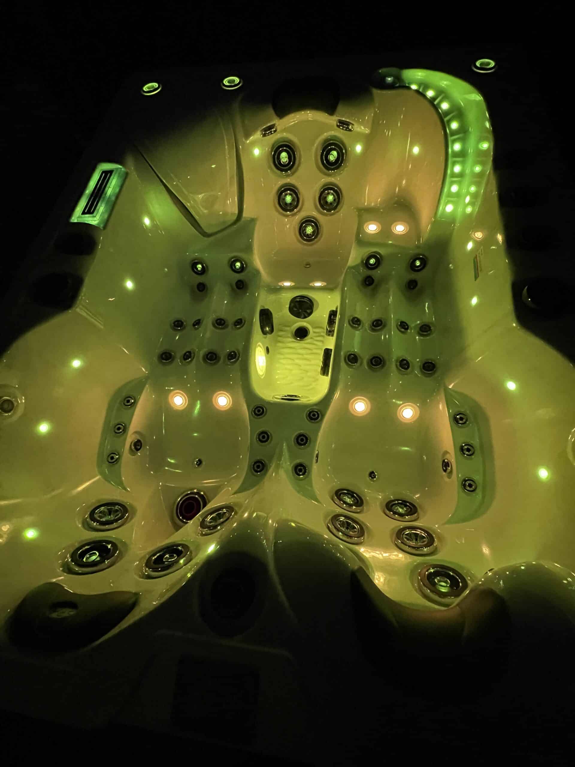 Jacuzzi haut de gamme éclairé en vert vibrant (chromothérapie) la nuit. Vue sur les sièges ergonomiques, les jets de massage et la cascade LED.