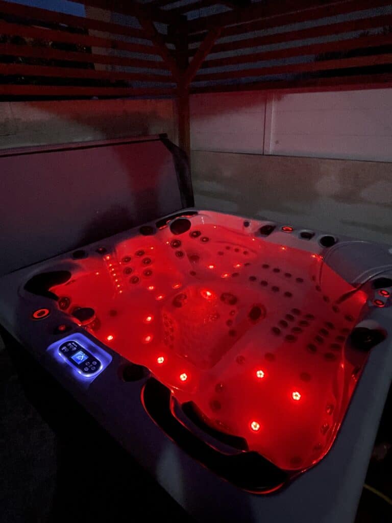 Jacuzzi de luxe : ambiance rouge LED intense la nuit Spa de luxe éclairé en rouge vif la nuit, avec un panneau de contrôle Balboa bleu affichant 35.0. Ambiance de détente.