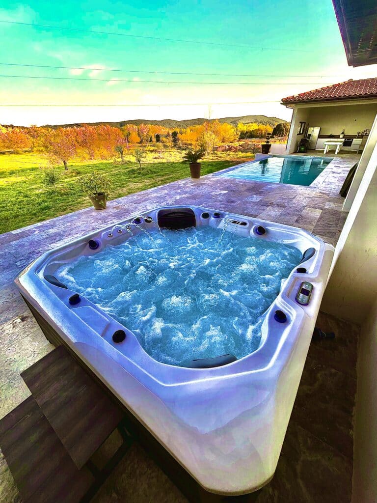 Spa Jacuzzi et Piscine de luxe avec vue sur la campagne. Grand jacuzzi bouillonnant sur une terrasse luxueuse, près d'une piscine à débordement, avec une vue colorée sur la campagne et les collines.