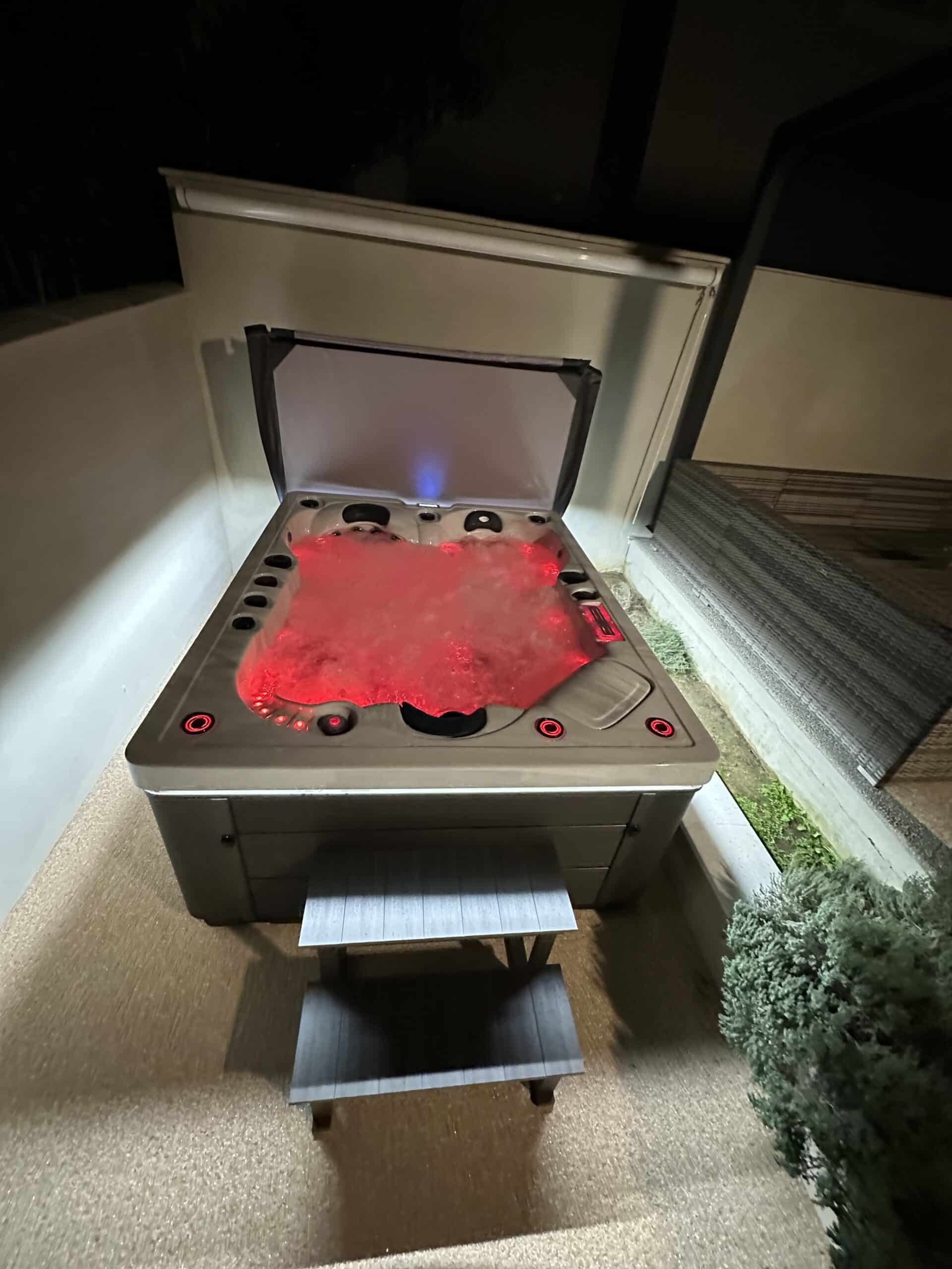 Spa d'extérieur rectangulaire avec marches, éclairage LED rouge vif et bulles. Ambiance chaude et relaxante au milieu de la nuit.