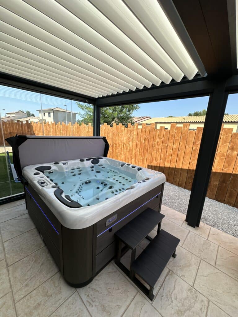 Spa Vendôm extérieur : luxe et relaxation sous pergola. Spa Vendôm extérieur moderne avec éclairage LED bleu sous une pergola bioclimatique. Terrasse carrelée et clôture en bois naturel.