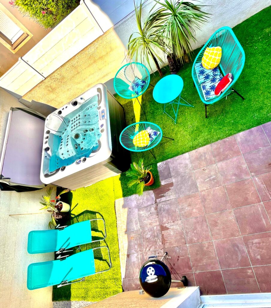 Détente tropicale : Spa, jacuzzi et mobilier turquoise. Terrasse de détente tropicale avec spa/jacuzzi, entourée de gazon synthétique. Mobilier turquoise (chaises Acapulco et transats) et coussins colorés.